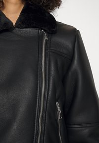 Zwarte leren jas met een zachte zwarte leren kraag, diagonale ritsdetails en een gestructureerde afwerking, met een extra ritszak aan de zijkant.