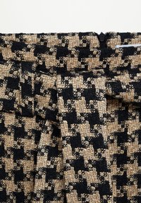 Tessuto con motivo a spina di pesce nero e beige con finitura testurizzata; presenta una vita arricciata con passanti per cintura e chiusura a cerniera.