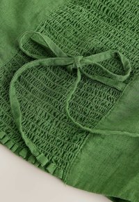 Tissu vert avec couture smockée et un détail de nœud noué sur une section texturée et froncée du vêtement.