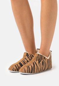 Tan slippers med svart tigerstripemønster, myk innvendig fôr og rund tå, med lav skåring og slip-on design.