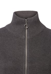 Grijze geribbelde gebreide trui met een hoge kraag en zilveren rits. De textuur is dik en warm, met horizontale ribbels voor extra detail.