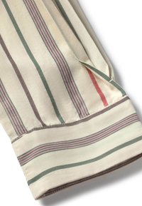 Manche d'une chemise en tissu beige avec des rayures verticales vertes, mauves et rouges, montrant un poignet et une partie d'une couture latérale.