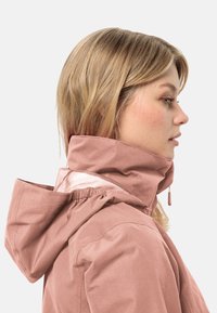 Light pink hooded jacket with a high collar, featuring a cinched neckline and mesh detailing at the back. Smooth fabric texture.