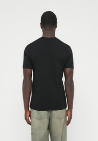 Črna bombažna majica s kratkimi rokavi in okroglim izrezom, prikazana od zadaj, kombinirana s svetlo sivimi kavbojkami.