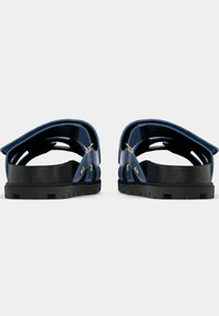 Μπλε σανδάλια με λαστιχένια σόλα και υφή μαύρο πάτο. Διαθέτουν διπλούς ιμάντες με χρυσές μεταλλικές λεπτομέρειες. Ανοιχτός σχεδιασμός στο πίσω μέρος.