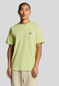 T-shirt in cotone verde chiaro con vestibilità rilassata, maniche corte e un piccolo logo ricamato nero sul petto.