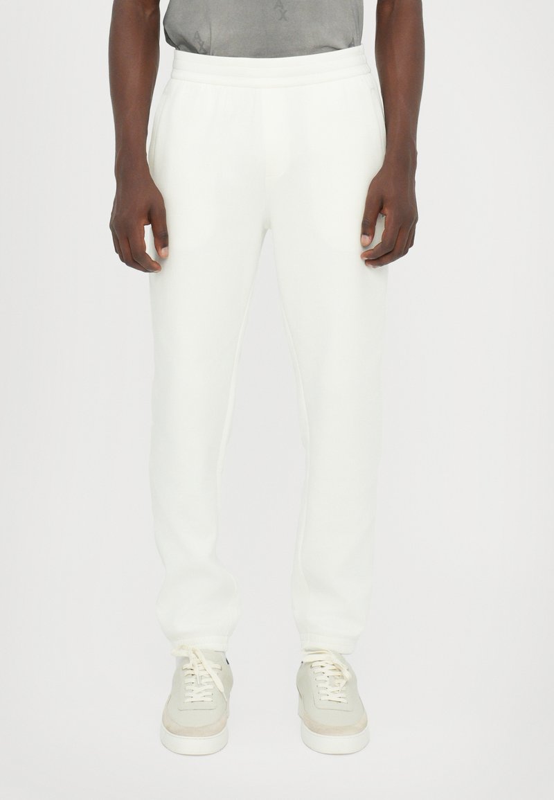 Witte jogbroek van zachte stof met een relaxte pasvorm. Voorzien van een elastische tailleband en boorden. Gecombineerd met lichtgekleurde sneakers.