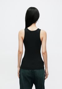 Fekete ujjatlan trikó puha anyagból, kerek nyakkivágással és testre szabott kialakítással, bő zöld farmernadrággal párosítva.