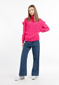 Rózsaszín, kötött turtleneck pulóver fodros vállbetétekkel, széles lábú kék farmernadrággal és fehér sneakerekkel párosítva.