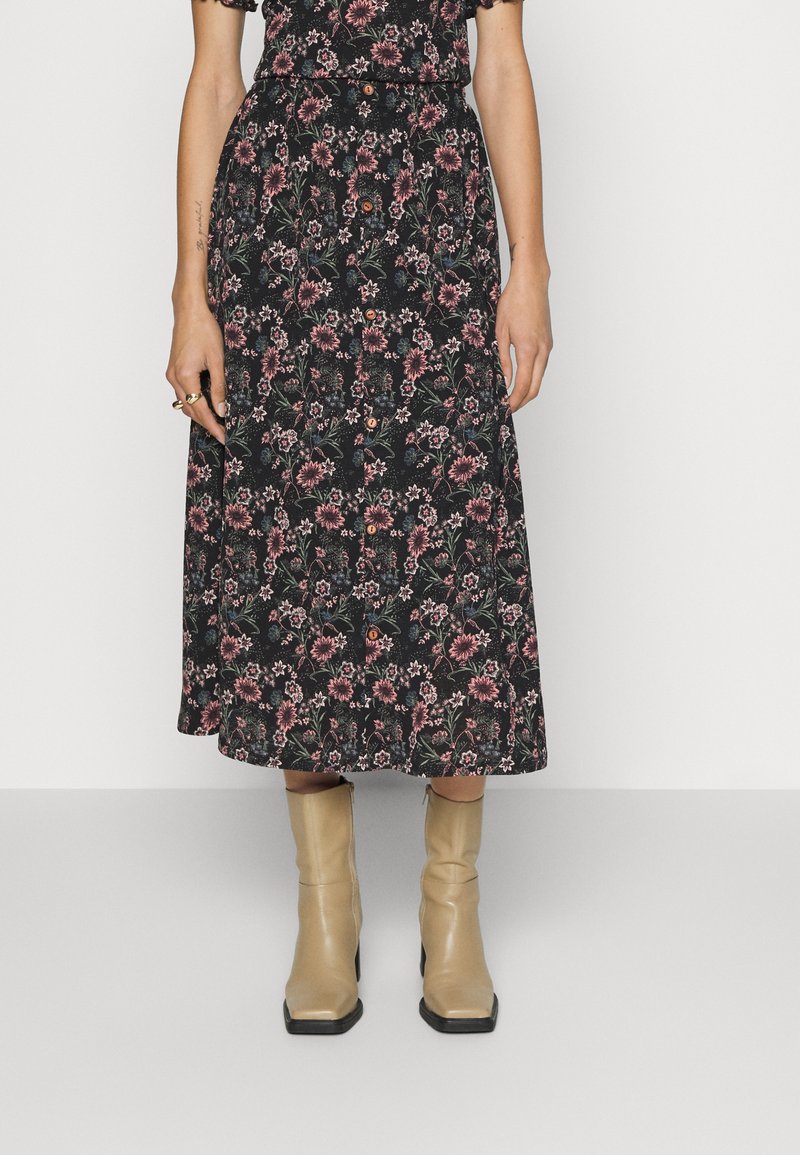 Saia midi preta com padrão floral em rosa e verde, com detalhes em botão, combinada com botas de tornozelo bejes.