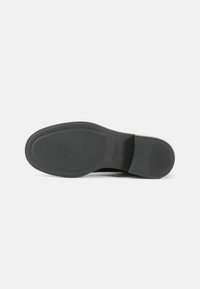 Suela de zapato de goma negra con una superficie texturada, un ligero arco, punta redondeada y un borde limpio a lo largo del talón.