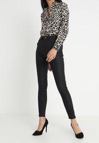 Blůza s leopardím potiskem a dlouhými rukávy, černé skinny džíny s vysokým pasem a černé lodičky na špičku. Hladký materiál a přiléhavý střih.