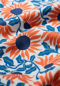 Kokvilnas audums ar ziedu rakstu, kurā ir apelsīnu ziedlapiņas, tumši zilas centra daļas, zaļas lapas uz baltas fona, ar teksturētu virsmu.