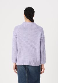 Pull en maille lavande clair avec un tissage texturé, épaules tombantes et ourlet côtelé. Présente une coupe décontractée et des manches longues.