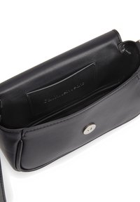 Černá kožená kabelka přes rameno s hladkou texturou, zapínáním na patentní knoflík a jednoduchým, obdélníkovým designem. Vnitřek obsahuje označení značky.