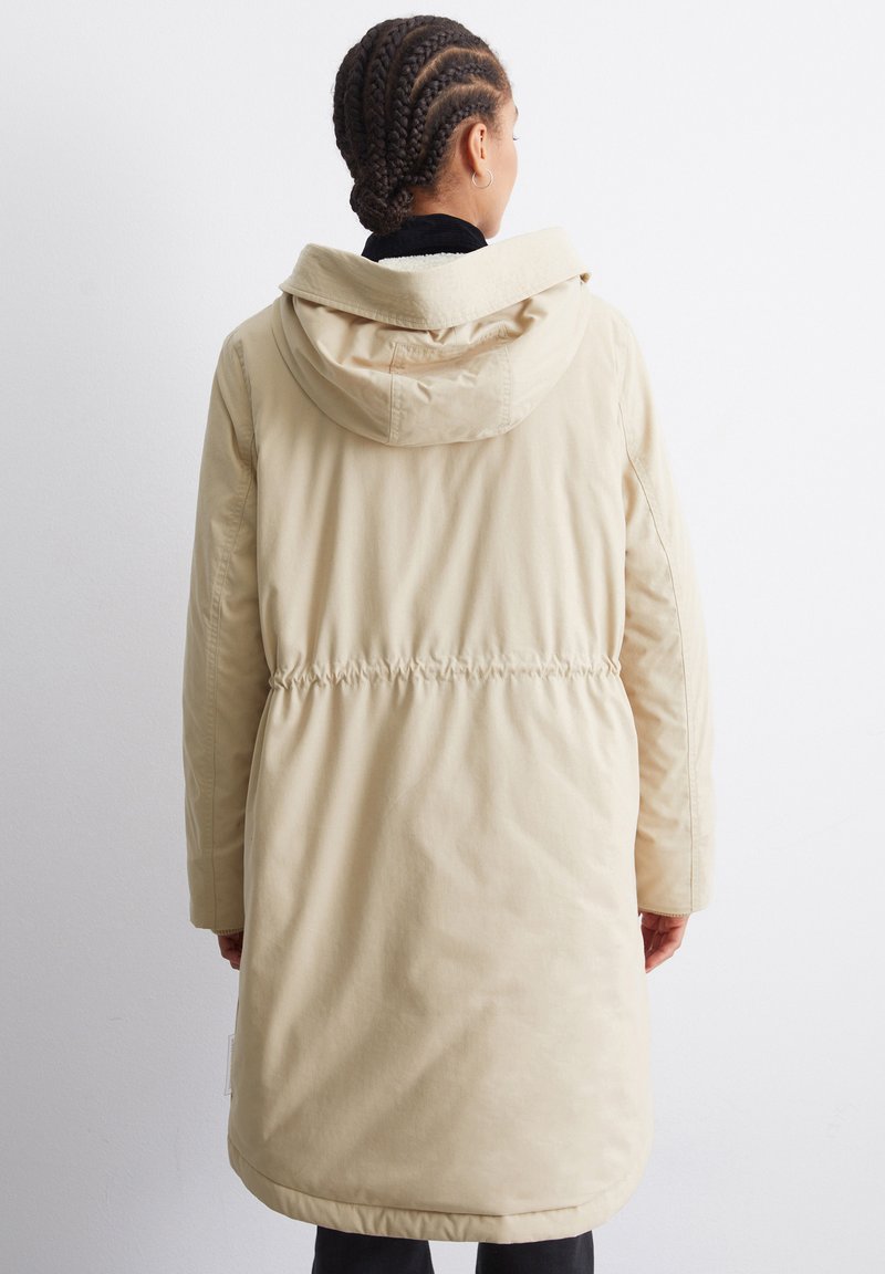 Langer beiger Parka mit Kapuze, tailliertem Schnitt und seitlichen Taschen. Weiche, glatte Textur mit einem schlichten Design und minimalen Details.