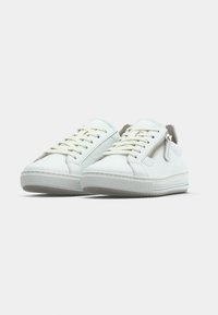 Paire de baskets basses blanches avec lacets et détail de fermeture éclair latérale sur fond neutre.