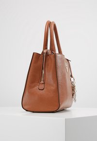 Sac à main en cuir marron de forme structurée, avec une fermeture éclair supérieure, des poignées doubles et un porte-clés suspendu.