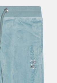 Svetlik blue velour hlače s pasom iz rebraste tkanine in srebrnim okovjem. Na strani je logo okrašen z rhinestones.