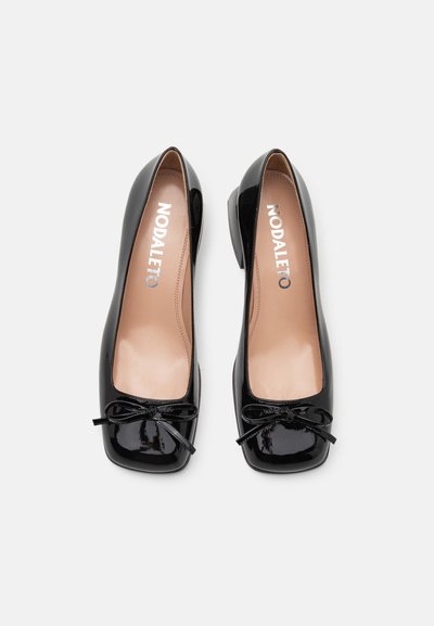 Schwarze Lackleder Ballerinas mit quadratischer Zehenpartie, kleinen Schleifendetails vorne und einem niedrigen Blockabsatz. Innensohle in Nude.