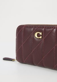 Burgundy leather wallet with diamond quilted texture, gold-tone hardware featuring a 'C' logo, and contrasting stitching detail.