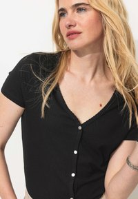 Haut court noir à côtes avec un décolleté en V, fermeture à boutons à l'avant avec des accents argentés, et tissu texturé.