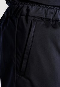 Pantaloni sportivi neri con vita elastica, tasche laterali e una superficie liscia e opaca. Design semplice e funzionale.
