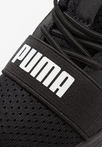 Black athletic shoe featuring a breathable mesh upper with textile accents. Prominent white "PUMA" logo on the elastic strap across the midfoot.