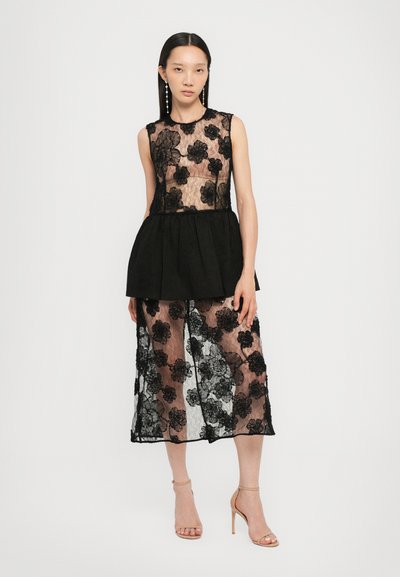 Top de encaje con diseño floral, peplum en capas, tejido negro transparente, falda transparente a juego. Incluye tirantes finos y tacones en tonos neutros.