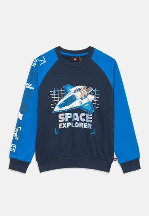 Jūras zilas un spilgti zilas krāsas sporta krekls ar kosmosa kuģa grafiku un uzrakstu "SPACE EXPLORER", kā arī ar kosmosa tematiku apdrukām uz kreisā piedurknes.