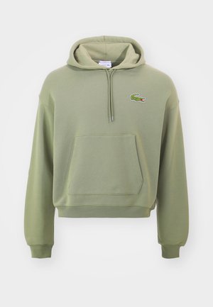 Sudadera verde corta hecha de tela suave, con un bolsillo tipo canguro y capucha con cordón, que presenta un pequeño logotipo bordado en el pecho.