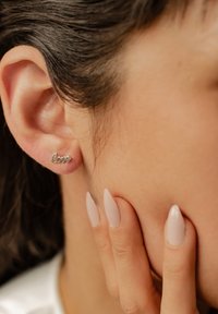 Pendiente de plata en forma de la palabra "amor". Llevado en el lóbulo, presenta una textura suave y un delicado diseño en cursiva.