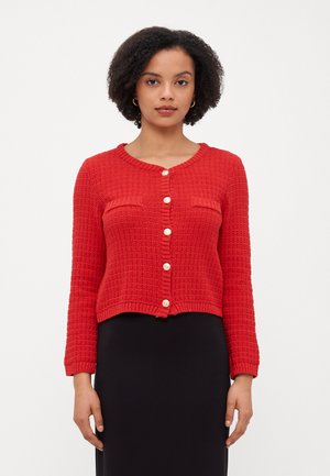 Cardigã tricotado em vermelho com um padrão texturado, gola redonda e fecho com botões. Apresenta dois bolsos frontais e uma bainha cropped.