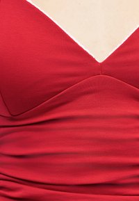 Κοντινό πλάνο ενός ατόμου που φοράει κόκκινο ρούχο με V-λαιμόκοψη, με μια λεπτή λευκή επένδυση κατά μήκος της λαιμόκοψης και ομαλή υφή υφάσματος.