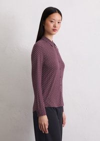 Chemise à boutons dans un bordeaux profond avec un motif géométrique. Manches longues, détail de col et ourlet droit. Assortie à un pantalon noir.