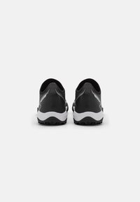 Un par de zapatillas deportivas negras con suelas blancas, vistas desde atrás, sobre un fondo blanco liso.