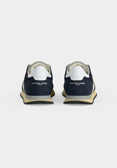 Paire de baskets bleu marine et blanches avec « PHILIPPE MODEL PARIS » sur les talons, vues de dos sur un fond clair uni.