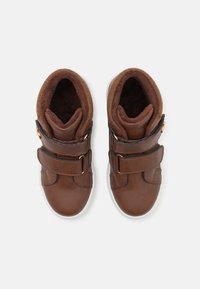 Brązowe skórzane sneakersy z dwoma regulowanymi paskami. Miękka brązowa podszewka, okrągły czubek i biała gumowa podeszwa. Gładka faktura z minimalnymi akcentami.