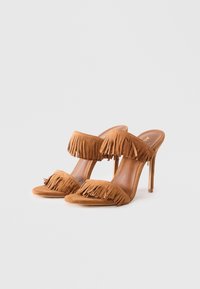 Tan suede heeled sandals featuring multiple fringe details on the straps, open toe design, and slim stiletto heel.