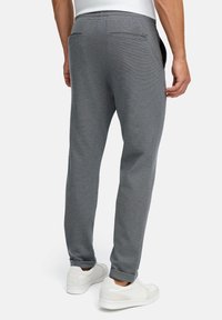Graue Jogginghosen mit strukturiertem Strick, schmal zulaufendem Bein, elastischem Bund und Gesäßtaschen, kombiniert mit weißen Turnschuhen. Schlichtes und funktionales Design.