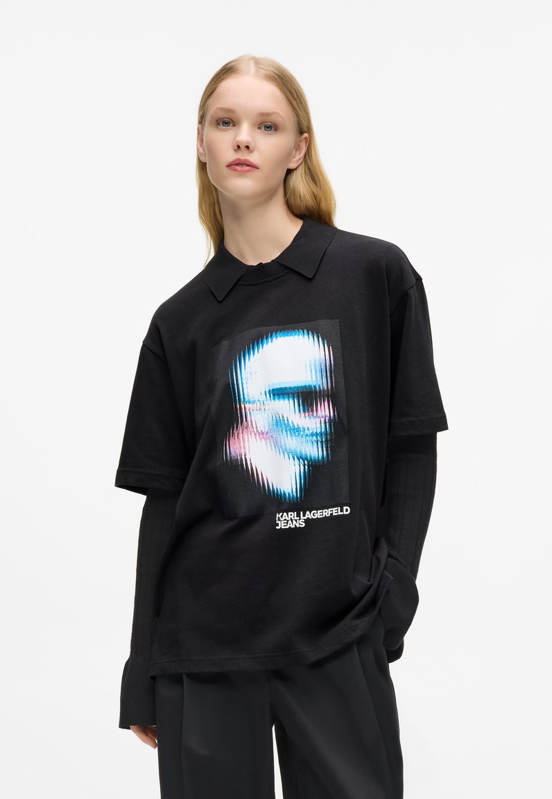 Melna kokvilnas T-kreklu ar grafisku dizainu stilizētai sejai zilos un rozā toņos, ar apkaklīti un brīvu piegriezumu.