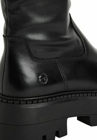 Černá kožená kotníková bota s hladkým povrchem, vybavená silnou platformovou podrážkou a kruhovým logem blízko švu.