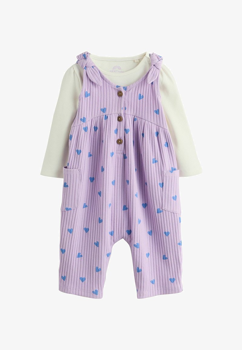 Grenouillère bébé côtelée violette avec impressions de cœurs bleus, boutons devant, poches et bretelles nouées sur une chemise à manches longues crème.