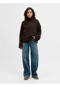 Maglione nero di pizzo con polsini a coste, abbinato a pantaloni in denim blu a gamba larga e scarpe marroni, su uno sfondo bianco semplice.