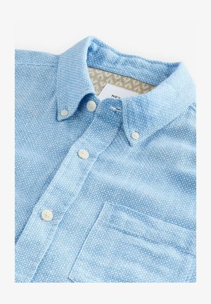 Chemise bleu clair à manches longues en tissu texturé, dotée d'un col, d'une poche poitrine et d'une doublure intérieure à motif subtil.
