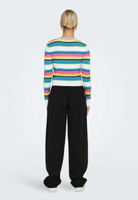 Maglione a maglia a righe multicolori con linee orizzontali in rosa, blu e bianco; abbinato a pantaloni neri larghi e sneakers bianche.