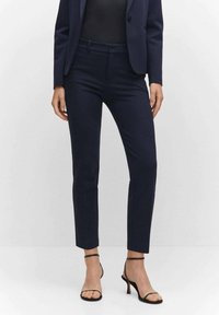 Pantalons ajustés bleu marine, en tissu lisse, avec une taille classique, associés à des talons noirs à lanières.