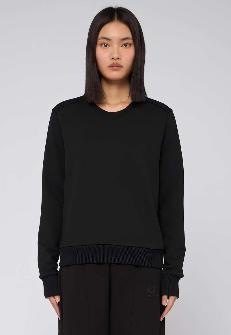 Svart sweatshirt med långa ärmar, ribbad halsringning och mudd, slät textur. Har en minimalistisk design utan synliga logotyper eller mönster.