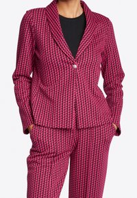 Růžový blazer s kostkovaným vzorem hounds-tooth, s klopovým límcem a zapínáním na jeden knoflík. Texturovaná látka, v kombinaci s odpovídajícími kalhotami.
