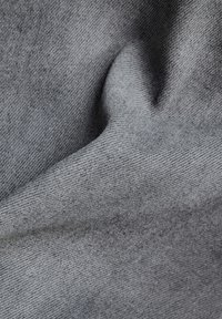 Artimos plano švelnios, tekstūruotos pilkos medžiagos su matomomis audimo detalėmis ir natūraliais raukšlėmis, kuriuose susidaro švelnūs šešėliai.